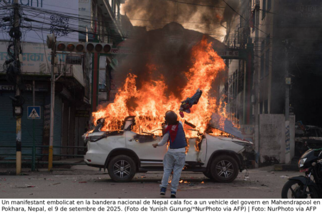 Un manifestant embolicat en la bandera nacional de Nepal cala foc a un vehicle del govern.